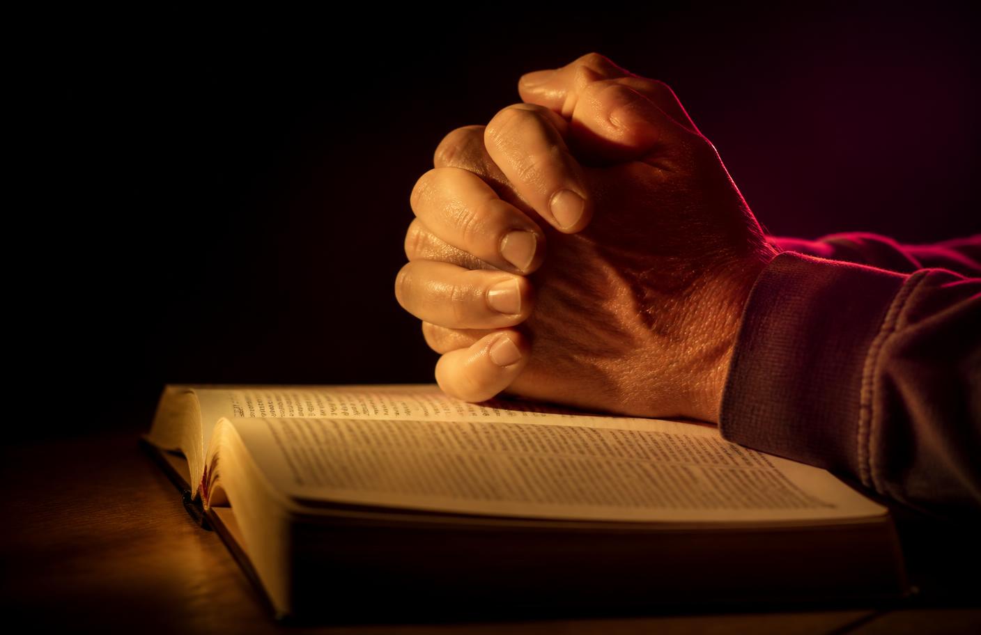 Hands clasped in prayer over an open Bible in warm gold light